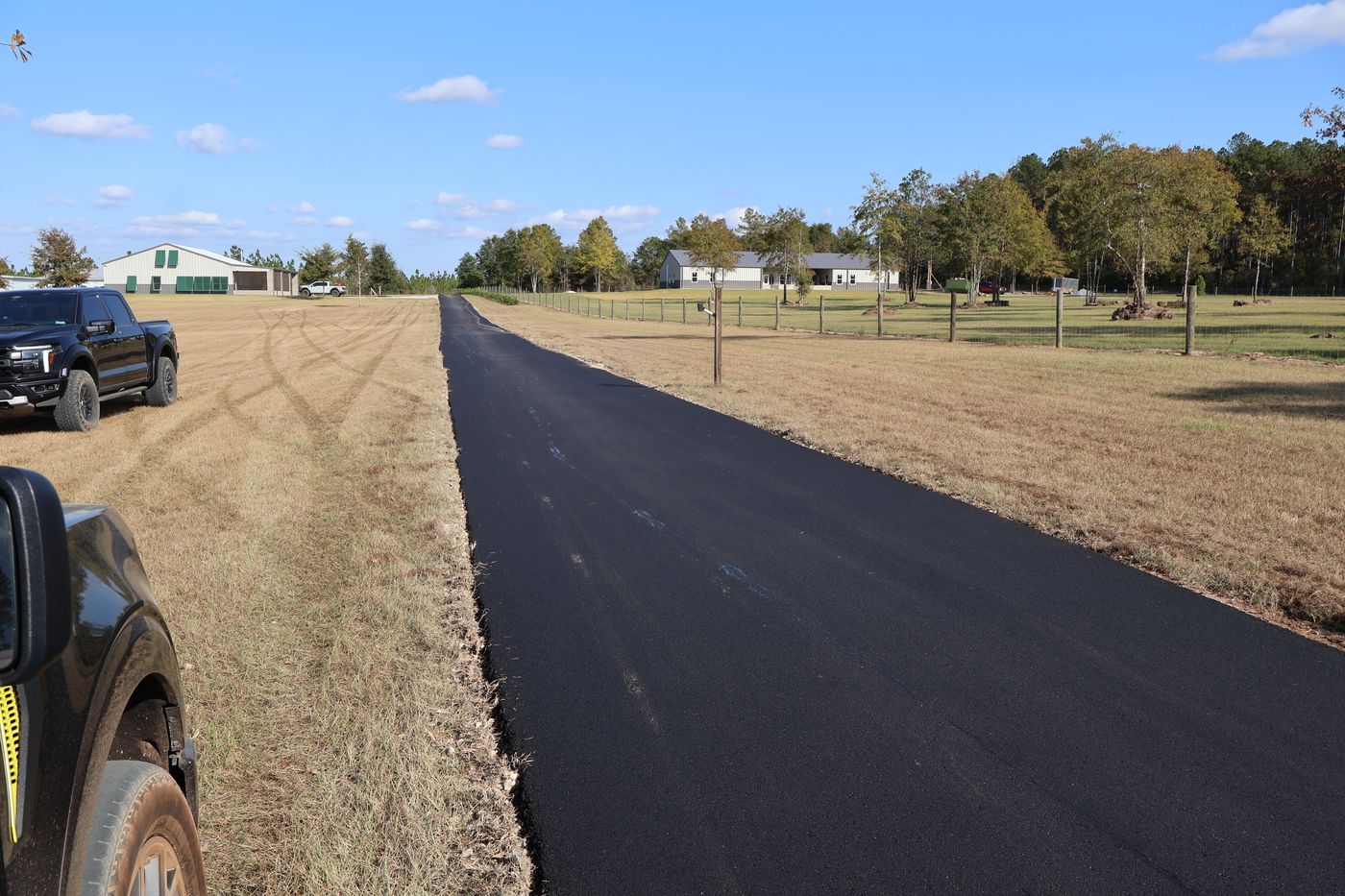 Long fresh asphalt driveway stretching between fields