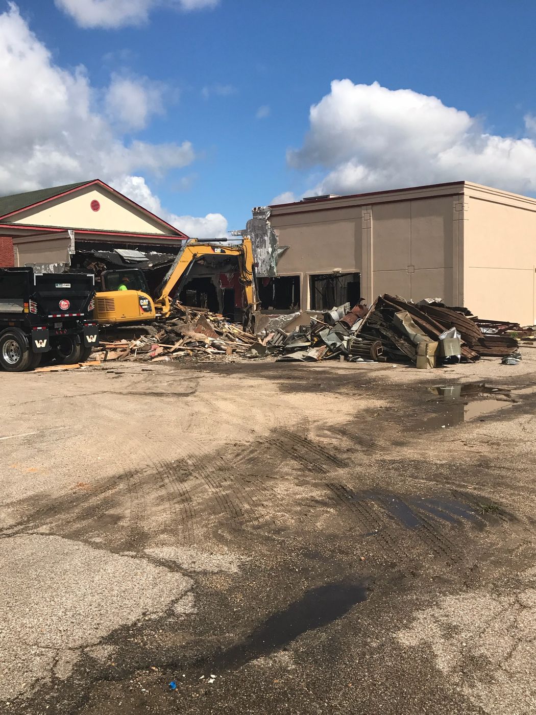 Excavator demolishing a commercial building with debris being loaded