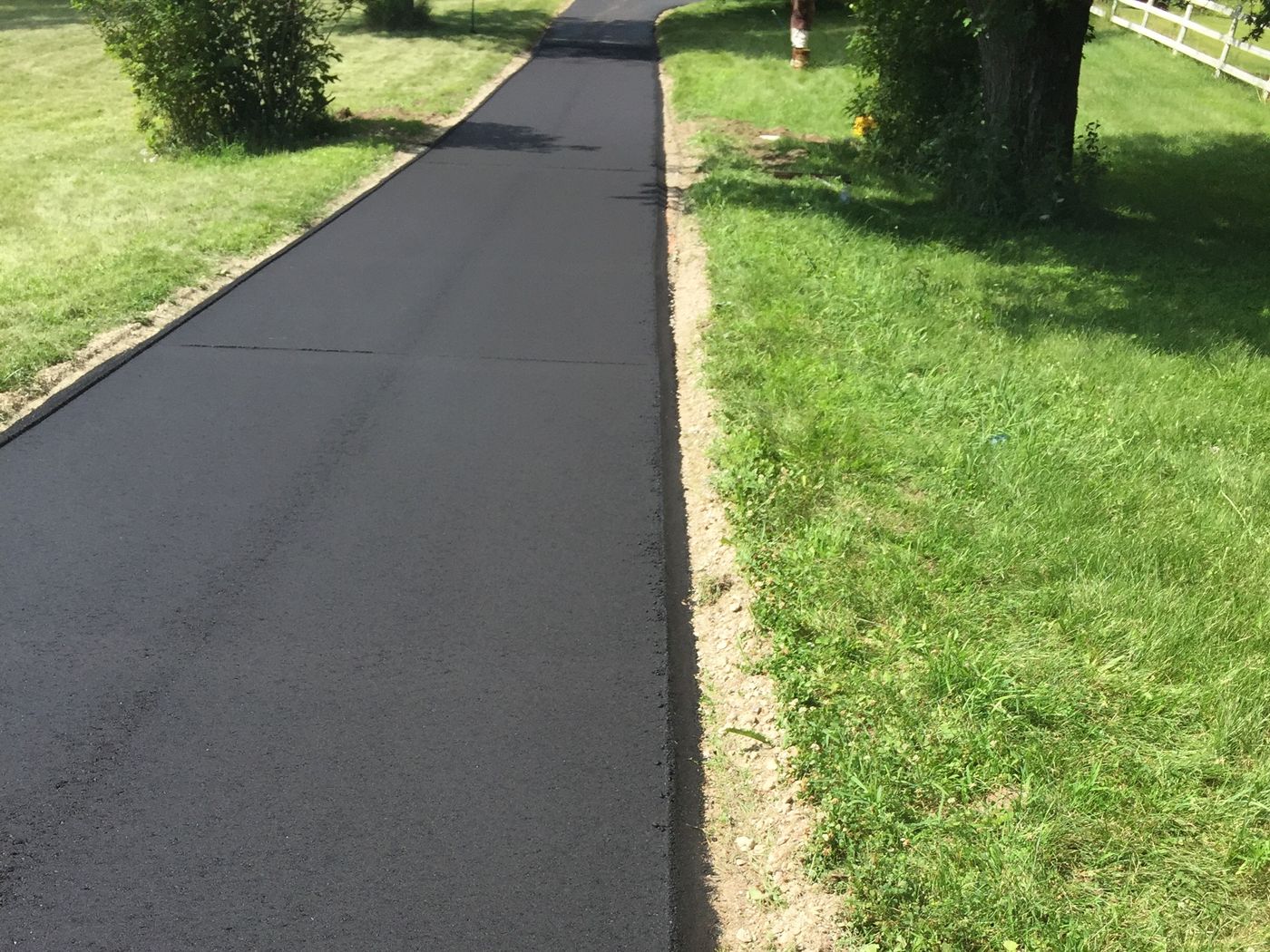 Long fresh asphalt driveway running between mown grass with a clean edge