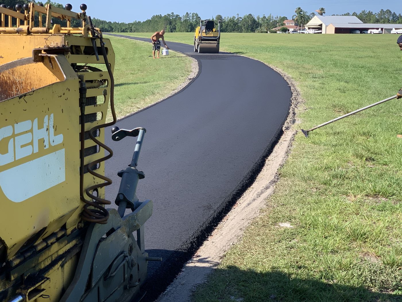 Paver and roller laying a sweeping curve of fresh asphalt on a private drive