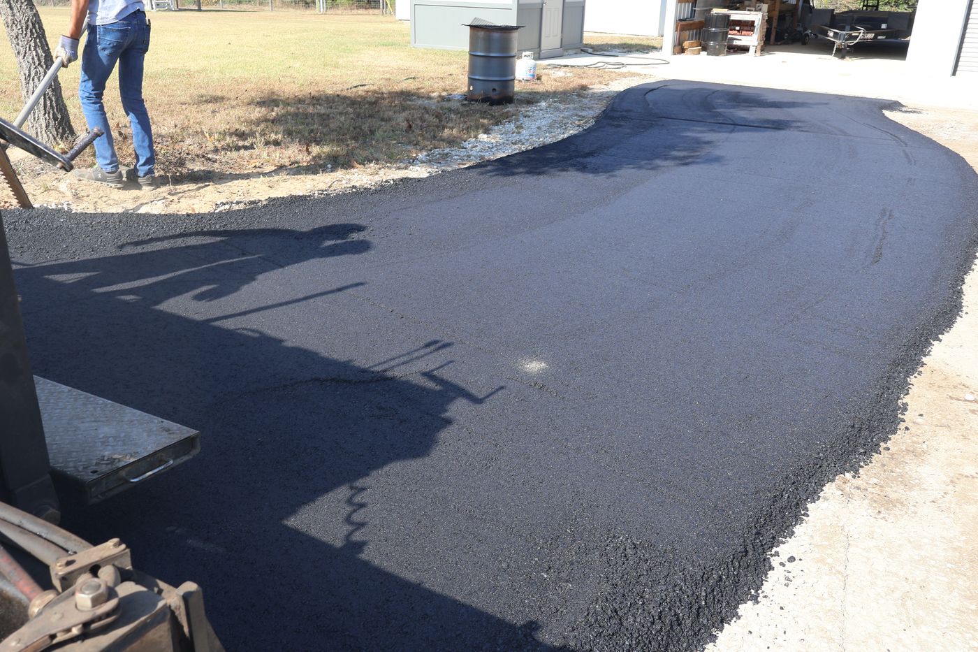 Fresh black asphalt driveway curving past a shop building